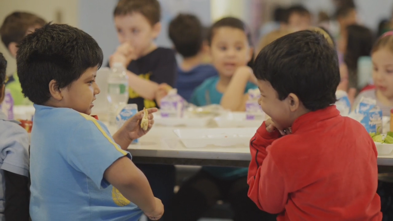 Elementary age students sitting at a lunchroom table eating and talking