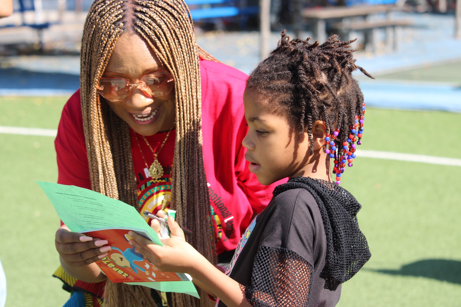 an adult and child at an outside event looking at a paper together