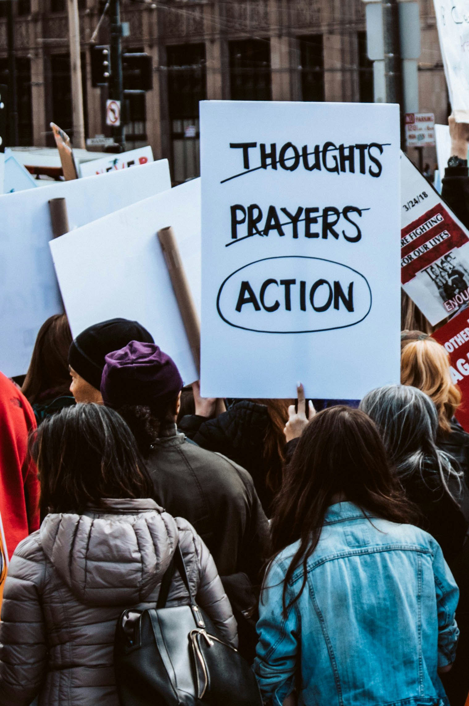 protest and a sign that says thoughts prayers action with thoughts and prayers crossed out and action circled